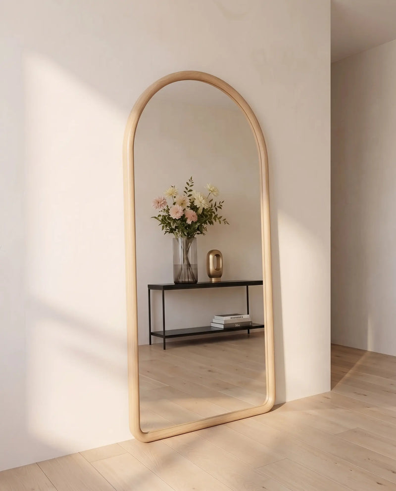 Pure No.1 houten boogspiegel in licht hout, schuin geplaatst in een lichte hal