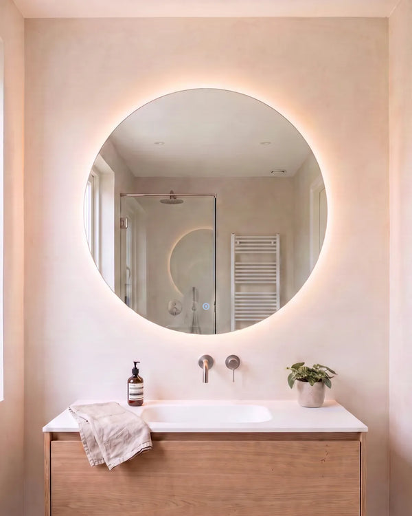 Ronde Lume Sol spiegel met LED verlichting in een lichte badkamer met roze stuc en eiken meubel